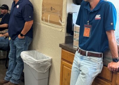 Gallery 62 Two men in blue shirts standing in an office, one leaning against a counter, the other near a wall.