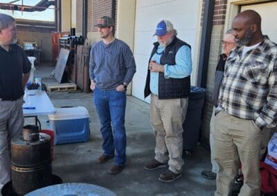 Gallery 74 Group of five men inspecting equipment outdoors at a company event.