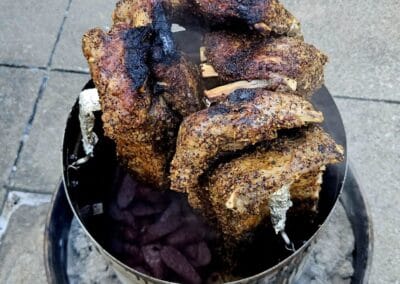 Gallery 82 Charcoal grilled meat on a skewer in a metal container with firewood underneath.