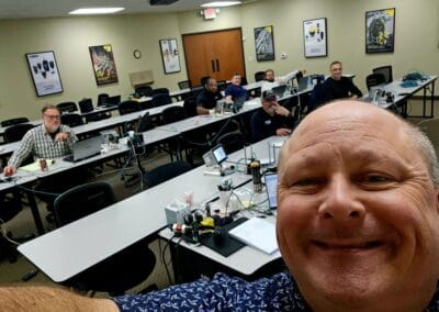 Gallery 84 Group of people in a training room with computers, led by a smiling instructor in the foreground.