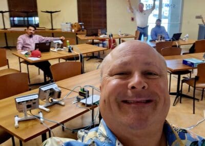 Gallery 88 Group of people in a classroom with electronic equipment, one person taking selfie.