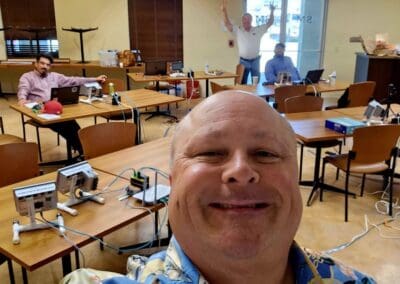 Gallery 89 Group of people in a classroom with electronic equipment and a man taking a selfie.