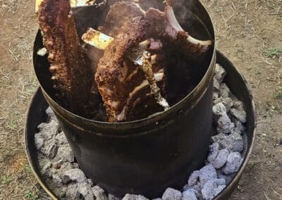 Gallery 91 Barbecue ribs cooking over open flame in a drum smoker with charcoal and wood.