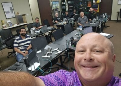 Gallery 96 Group of people in a classroom with computers and robotics equipment, smiling for a selfie.