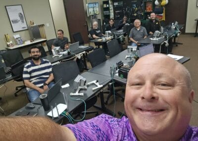 Gallery 97 Group of people in a classroom with computers, selfie taken by a man in a purple shirt.