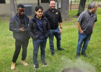 Gallery 102 Group of five men standing outdoors near trees and grass, some using smartphones.