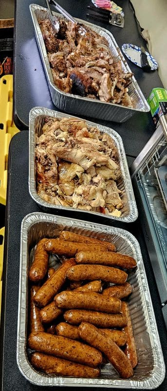 Gallery 107 Assorted grilled meats and sausages served in aluminum trays at a food event.
