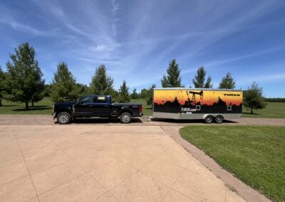 Gallery 11 Black pickup truck with TURKC.com trailer parked on a grassy area under blue sky.