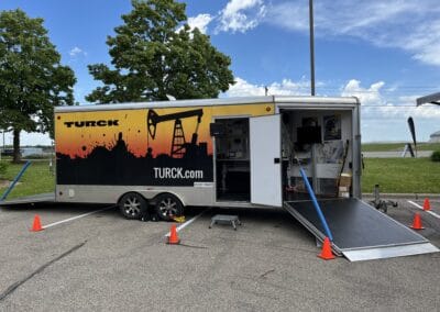 Gallery 13 Mobile oilfield equipment trailer with Turck branding and hydraulic ramp at outdoor site.