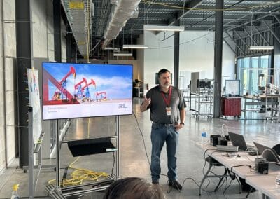 Gallery 19 Man giving presentation in industrial-style conference room with large screen showing oil rigs.
