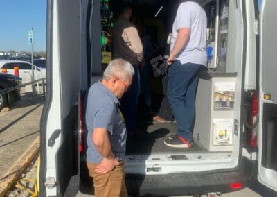 Gallery 33 Technicians inspecting equipment inside a mobile testing van at a parking lot.