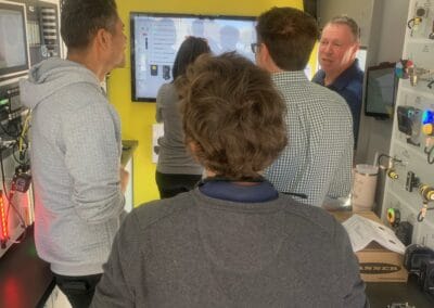 Gallery 34 Group of people in a tech demonstration room with a large screen and equipment.
