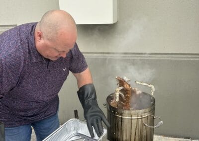 Gallery 40 Man grilling meat outdoors with smoke rising from a barrel grill near a wall.