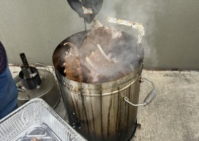 Gallery 42 Person grilling meat on a vertical smoker with smoke rising, outdoor setting.