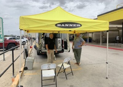 Gallery 50 Automated Dynamics Corp. outdoor promotional event with yellow tent and two staff members.