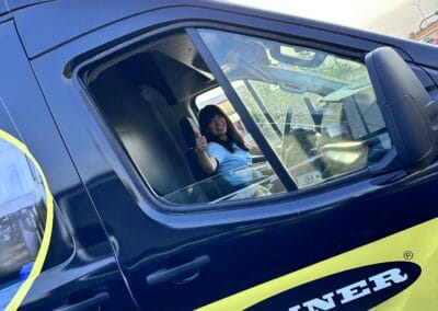 Gallery 54 Woman sitting in a blue and yellow Banner service vehicle, waving from the window.