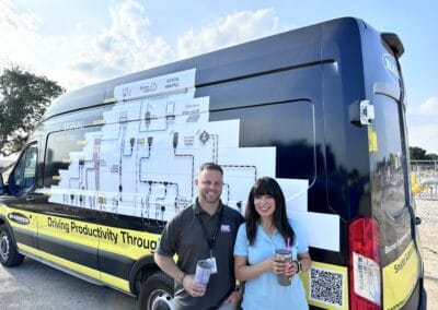 Gallery 55 Automated Dynamics Corp. mobile unit with two smiling staff members holding drinks, showcasing tech.